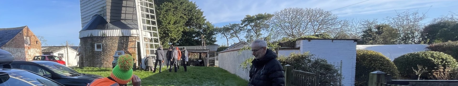 A man in a hi-viz vest uses a surveyors machine in front of a windmill