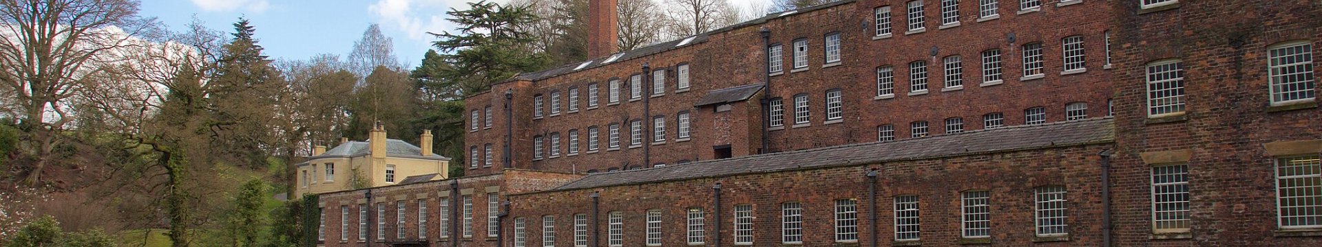 Exterior of Quarry Bank Mill with blue sky and clouds in background and grass in foreground
