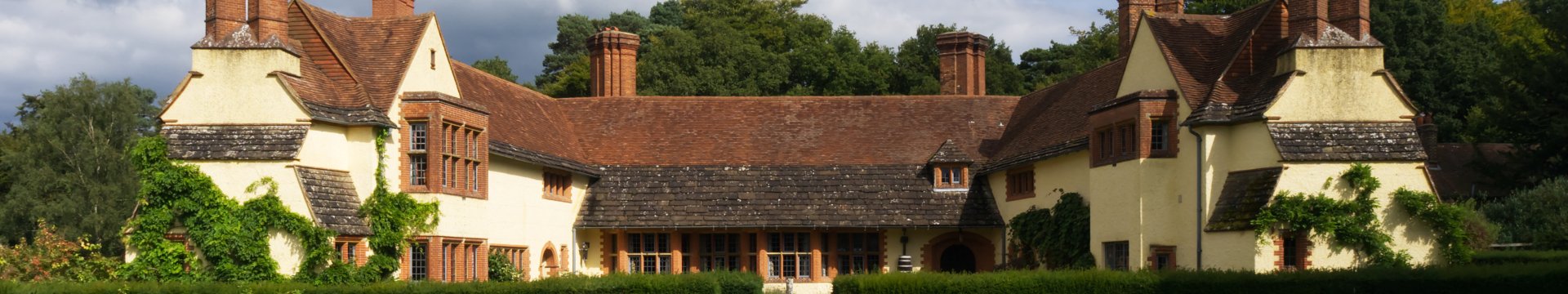 A large house with gable ends at left and right and a yard between the wings