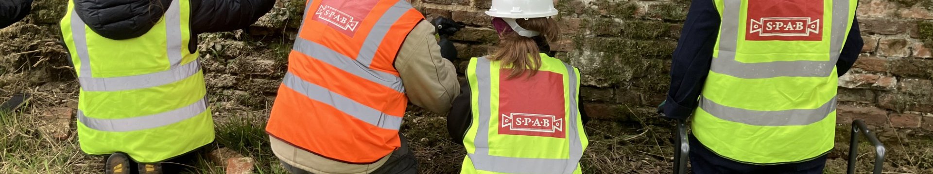 Tutor, Lynn Mathias wearing orange high vis vest and three women participants wearing yellow high vis vests, all kneeling while repointing historic brick wall at Hatfield House