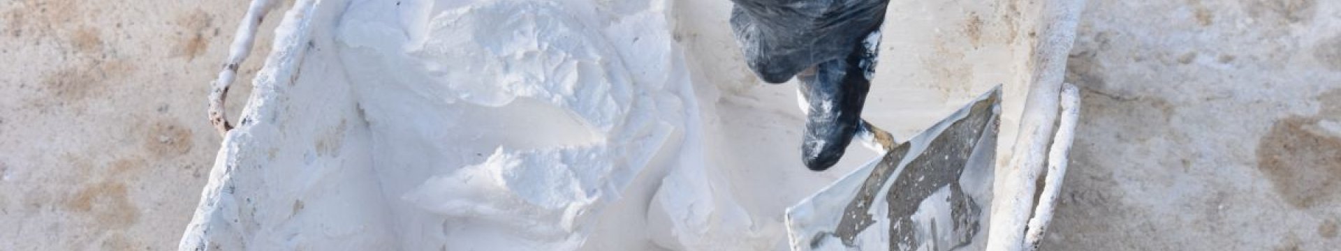 A square bucket frull of white lime product. A person is mixing it with a trowel.