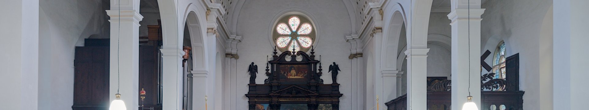 Interior of Church of St Thomas the Martyr in Bristol, facing east towards the 18th century reredos and showing with white walls and semi-circular arches and dark wooden pews. 