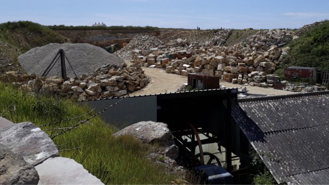 Exterior view looking across a quarry, showing stockpiles of quarried Purbeck stone, aggregate and working areas within the active limestone quarry