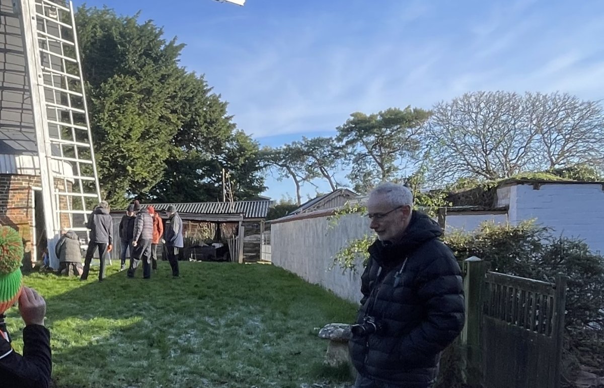 A man in a hi-viz vest uses a surveyors machine in front of a windmill