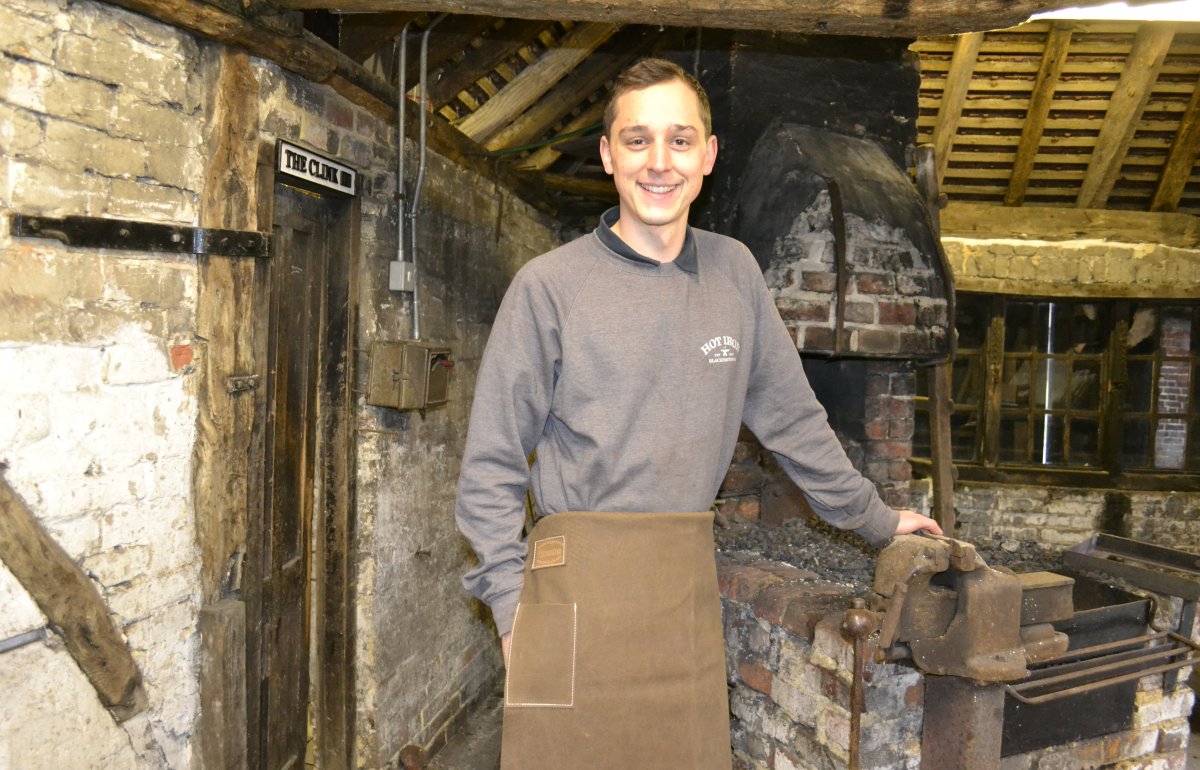 Henry Rogers smiling at the camera in front of the main forge inside Chiddingfold Forge