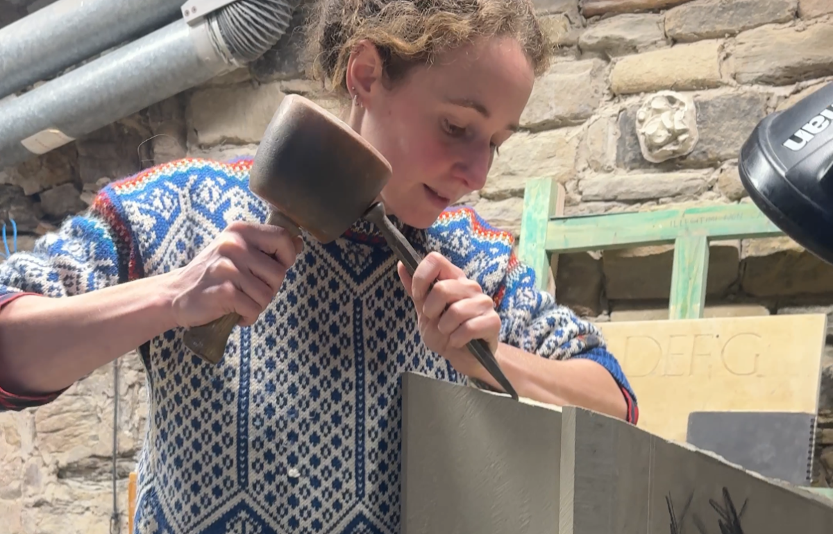 Grace Impesi working at stone masonry in a workshop. Using a hammer and chisel on a stone.